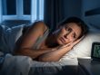 Person lying awake in bed at night with a soft glow from a bedside alarm, illustrating insomnia and trouble sleeping.