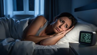 Person lying awake in bed at night with a soft glow from a bedside alarm, illustrating insomnia and trouble sleeping.