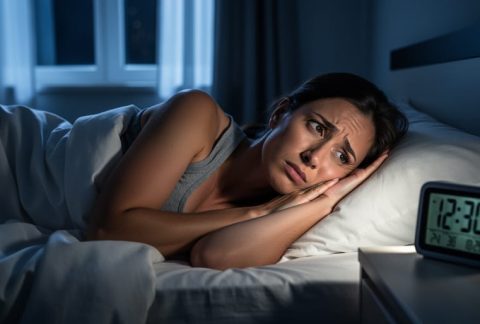 Person lying awake in bed at night with a soft glow from a bedside alarm, illustrating insomnia and trouble sleeping.