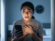Person clutching their chest and holding a phone in a softly lit room, expressing urgency and distress during a severe anxiety attack.