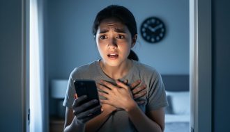 Person clutching their chest and holding a phone in a softly lit room, expressing urgency and distress during a severe anxiety attack.